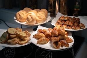 Croissant and bread on paper and white dish in the dark are decorated in tungsten light from lamp. photo