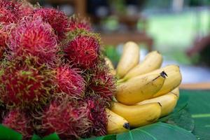 Banana and rambutan group on the artifact banana leaf on the table in outdoor garden. photo