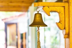 campana de latón con la mano en el palo grande de madera en la pared del poste. foto