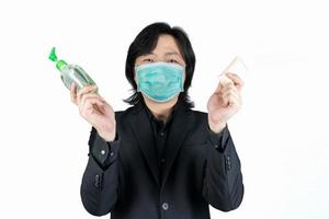 Asian man is holding and showing cleaning alcohol gel and soap on his hand and wear black mask on clear white background. photo