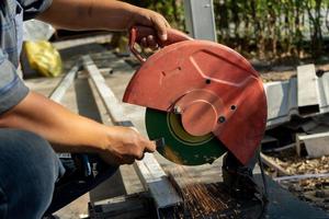 el trabajador de la construcción asiático está afilando el cincel con una máquina de cuchillas grandes en el campo al aire libre con un árbol en el fondo de la fila. foto