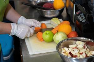 la mano de la mujer está cortando la zanahoria, la verdura y la fruta, como la manzana, la guayaba, la naranja, en el plato de plástico en la cocina del ambiente oscuro. foto
