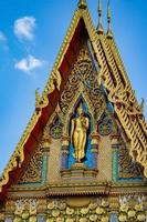 la estatua de buda se encuentra en la parte delantera del edificio del templo con un hermoso estilo de patrón de arte tailandés en el día de cielo abierto. foto