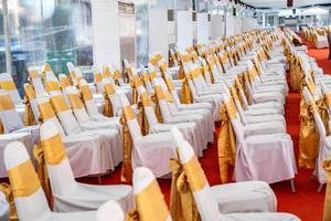 carpa interior con aire acondicionado temporal para eventos al aire libre en el día. el interior de las tiendas tiene una alfombra roja y muchas sillas cubiertas con tela blanca y una cinta dorada. foto