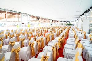 carpa interior con aire acondicionado temporal para eventos al aire libre en el día. el interior de las tiendas tiene una alfombra roja y muchas sillas cubiertas con tela blanca y una cinta dorada. foto