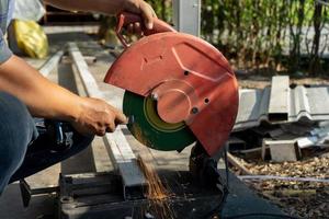 el trabajador de la construcción asiático está afilando el cincel con una máquina de cuchillas grandes en el campo al aire libre con un árbol en el fondo de la fila. foto