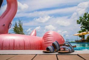 Vacation and leisure summer lifestyle by takeoff shoe laying beside pink flamingo beside th swimming pool at summer period. photo