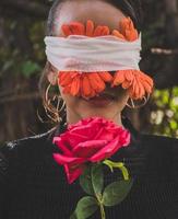 Woman with red flowers bandaged to her eyes with a rose in her hand photo