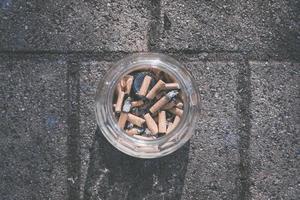 cenicero de cristal lleno de colillas de cigarrillos foto