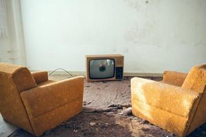 Pair of disused sofa chairs in front of broken TV photo