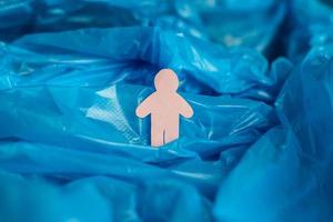 The silhouette of a man carved from pink paper is immersed in a blue plastic bag as if in waves of water, ocean, sea. photo