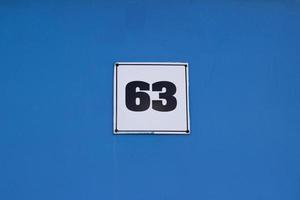 Metal plate with house number 63 black color on white. On a blue wall. The wall of the house photo