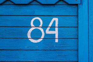 House number 84. The numbers are painted in white paint using a stencil on a wooden blue wall made of dry old planks. The wall of the village house photo