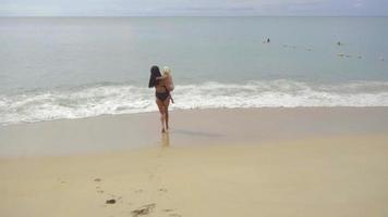 Young woman with a two year old daughter walking and sing a song along the sandy beach, slow motion video