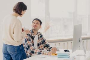 Family, paper work and technology concept. Husband and wife study contract agreement, read terms and conditions, discuss domestic bills, drinks coffee, man poses at desktop with modern computer photo