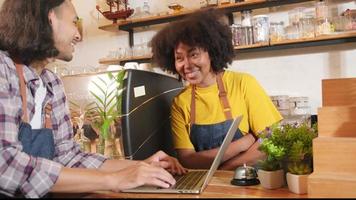 Two cafe business startup partners and friends, African American female, and Thai male baristas talk and cheerful smile together at counter bar of coffee shop, happy service job, and SME entrepreneur. video