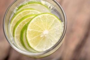 Close up top view green lime sliced in the soda water and glass place on the wooden table with blurred background photo