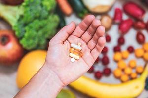 mano sujetando suplementos alimenticios sobre verduras y frutas para un estilo de vida saludable foto