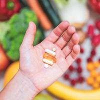 mano sujetando suplementos alimenticios sobre verduras y frutas para un estilo de vida saludable foto