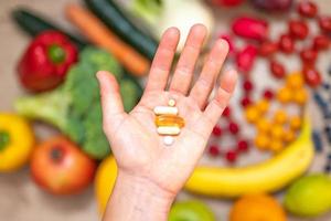 mano sujetando suplementos alimenticios sobre verduras y frutas para un estilo de vida saludable foto