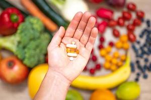 mano sujetando suplementos alimenticios sobre verduras y frutas para un estilo de vida saludable foto