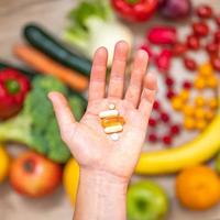 mano sujetando suplementos alimenticios sobre verduras y frutas para un estilo de vida saludable foto