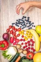 mano sujetando suplementos alimenticios sobre verduras y frutas para un estilo de vida saludable foto