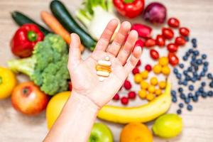 mano sujetando suplementos alimenticios sobre verduras y frutas para un estilo de vida saludable foto