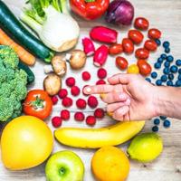Hand holding food supplements over vegetables and fruits for a healty lifestyle photo