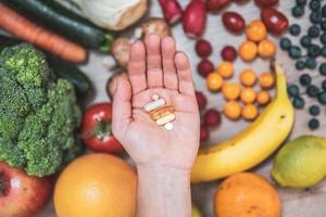 Hand holding food supplements over vegetables and fruits for a healty lifestyle photo