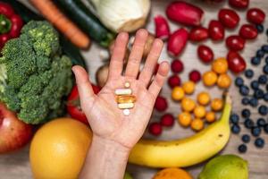 mano sujetando suplementos alimenticios sobre verduras y frutas para un estilo de vida saludable foto