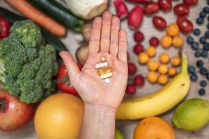 mano sujetando suplementos alimenticios sobre verduras y frutas para un estilo de vida saludable foto