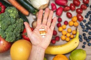 mano sujetando suplementos alimenticios sobre verduras y frutas para un estilo de vida saludable foto