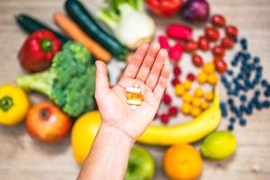 mano sujetando suplementos alimenticios sobre verduras y frutas para un estilo de vida saludable foto