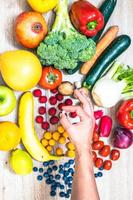 mano sujetando suplementos alimenticios sobre verduras y frutas para un estilo de vida saludable foto