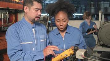 Asian male and female African American engineers in safety uniform work by inspecting machines' voltage current, checking, and maintaining at manufacture factory, electric system service occupations. video