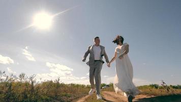 two lovers run holding hands in a field. A man runs after a woman on a dirt road in a field on a sunny day. video