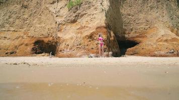una joven solitaria en la playa con traje de baño corre a nadar. playa de arena salvaje y una chica en la playa. video