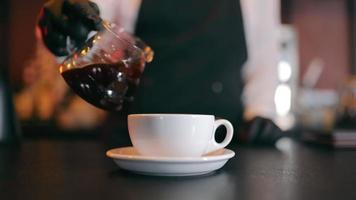 vertiendo café negro en una taza. camarero sirviendo café en una taza blanca en un restaurante. video