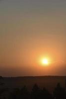 Orange sunset in the summer evening on the background of the forest and the circle of the sun. photo