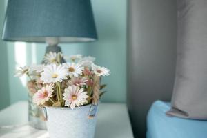 flores borrosas y la lámpara sobre la mesa con rayos de sol en el dormitorio foto