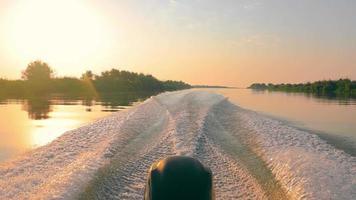 motorbootroutes op kalm rivieroppervlak bij zonsondergang. speedmotorboot die in het glanzende water van de rivier vaart en bij de zomerschemering witte wervelsporen achterlaat. concept van wateractiviteiten video