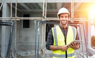 ingeniero civil o arquitecto profesional masculino usa casco de seguridad. ingeniero, inspector con tecnología de tabletas para el proyecto de construcción de listas de verificación en el sitio de construcción. mira la cámara con cara de sonrisa. foto