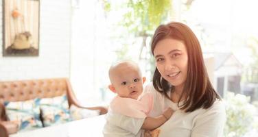 Happy family, Cute Asian newborn baby with young mother smile happy face. Innocent little infant adorable. Mom carrying, taking care with love indoor at home. Parenthood, mother day concept.