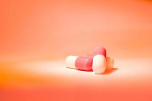 Three red white pill capsules in a slide on an orange background with a gradient. photo