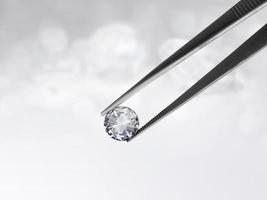 Dazzling diamond held in tweezers on a bokeh background photo