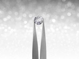brillliant round diamond in tweezer on white shining bokeh background. concept for chossing best diamond gem design photo