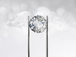 Dazzling diamond held in tweezers on a bokeh background photo