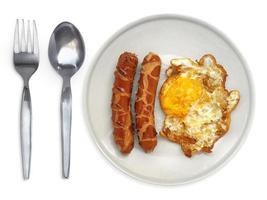 fried egg on a plate with spoon and fork sausage on a white background photo