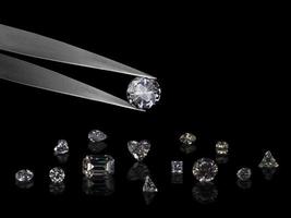 Diamond in tweezers on a black background with diamonds group soft focusing photo